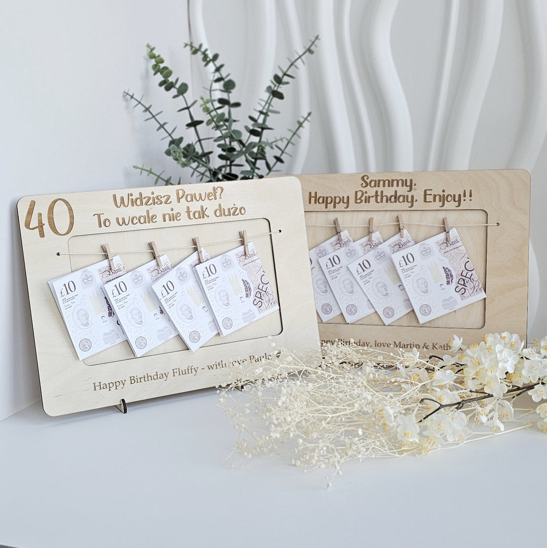 A wooden frame with a plant and flowers on a white surface, displaying a birthday wish list with money amounts and a message about a birthday celebration.