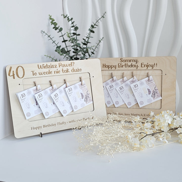 A wooden frame with a plant and flowers on a white surface, displaying a birthday wish list with money amounts and a message about a birthday celebration.