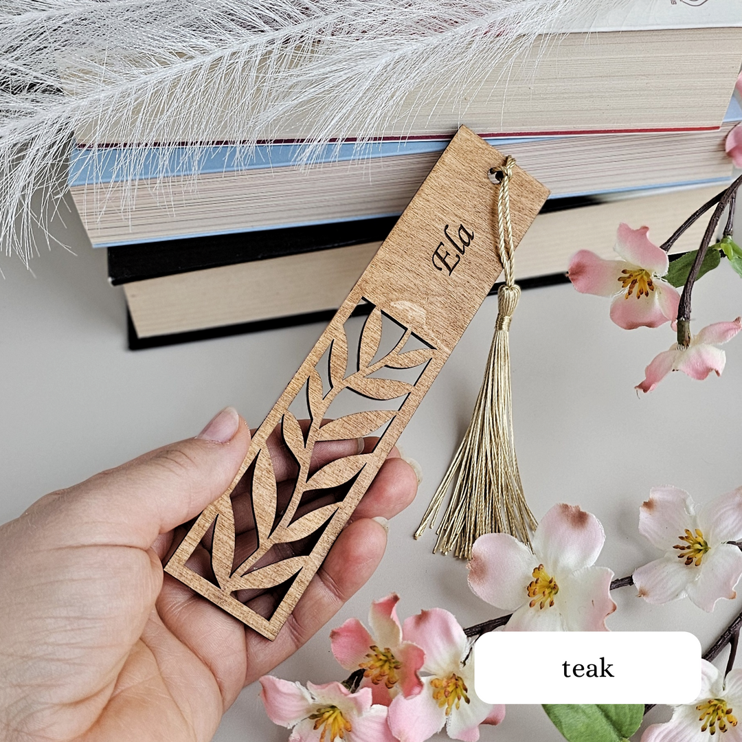 a hand holding a wooden bookmark with a tassel