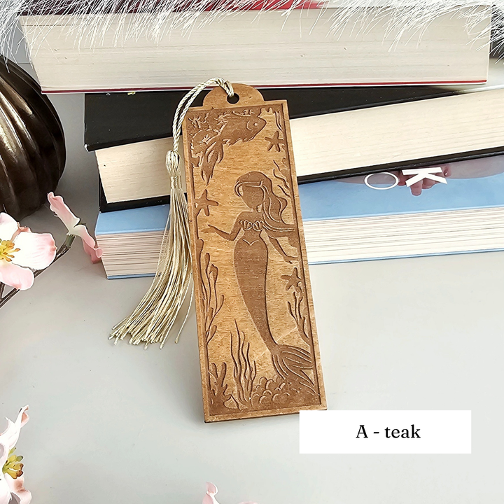 A wooden bookmark with a mermaid design, featuring a tassel, is placed on top of a stack of books.