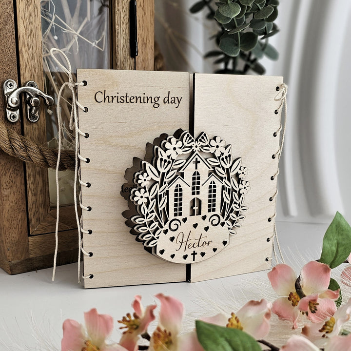 A wooden card with a decorative floral design and the name "Hector" on it, placed on a table with pink flowers.