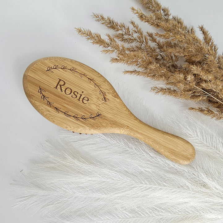 A wooden brush with the name "Rosa" engraved on it, placed on a white surface next to dried flowers.