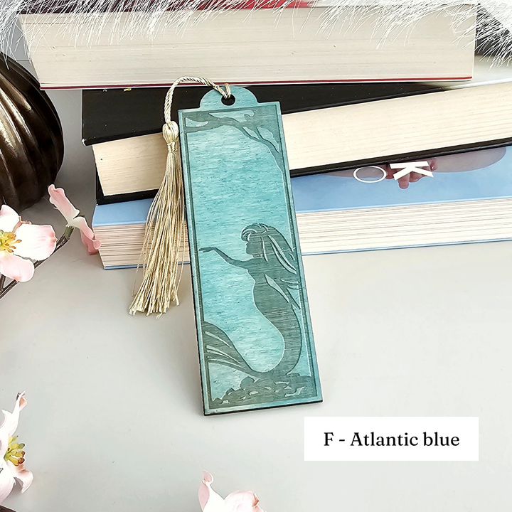 A turquoise-colored mermaid-themed bookmark with a tassel is placed on top of a stack of books.