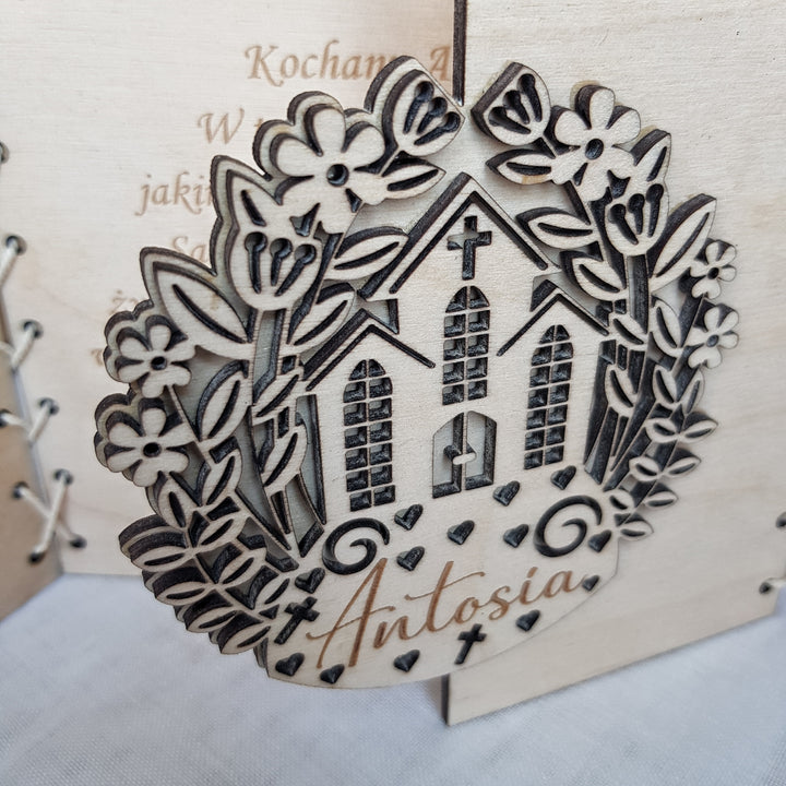 A wooden ornament with a church design and floral elements, featuring the name 'Antosia' engraved on it.