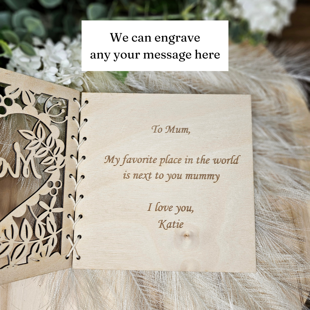 a wooden card with a heartfelt message engraved on it, placed on a surface with a floral pattern.