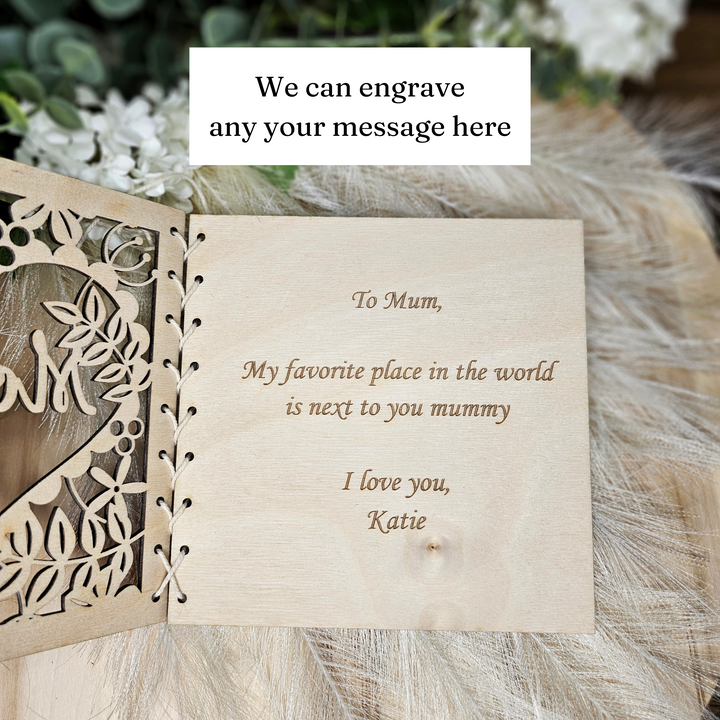 a wooden card with a heartfelt message engraved on it, placed on a surface with a floral pattern.