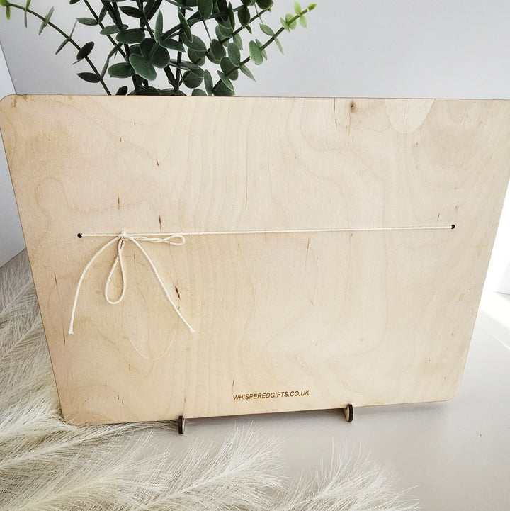 a wooden board with a white string tied around it, placed on a white surface. There is a plant in the background, and the board appears to be a display or presentation item.
