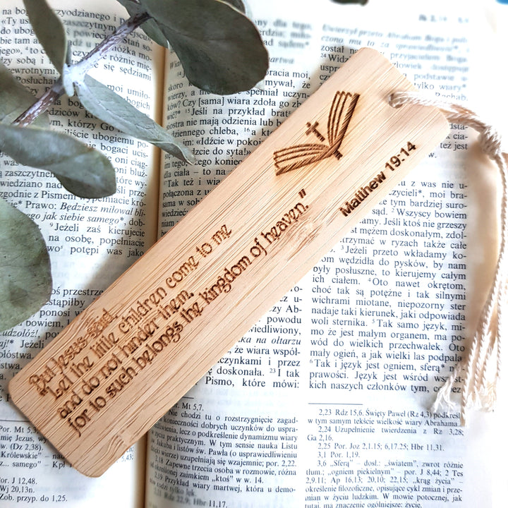 A wooden bookmark with a Bible verse engraved on it, resting on top of an open book with text visible.