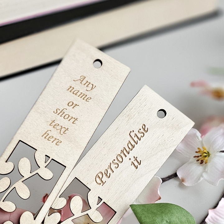 Two wooden bookmarks with personalized text engraved on them, placed on a surface with a blurred background.