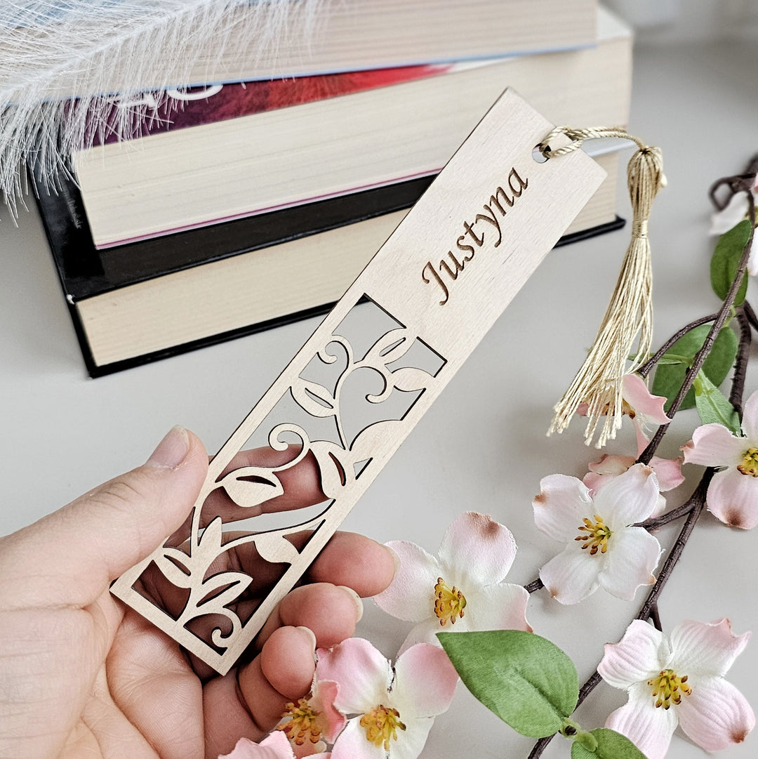 a person holding a bookmark next to some flowers