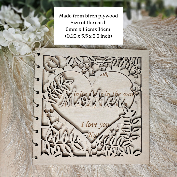 a wooden card with a heart-shaped cutout and the text "I love you" carved into it. The card is made from birch plywood and has a size of 6mm x 14cm x 14cm (0.25 x 5.5 x 5.5 inches).