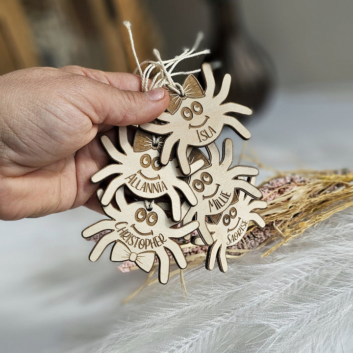 A hand is holding a group of wooden ornaments shaped like smiling faces, each with a name tag.