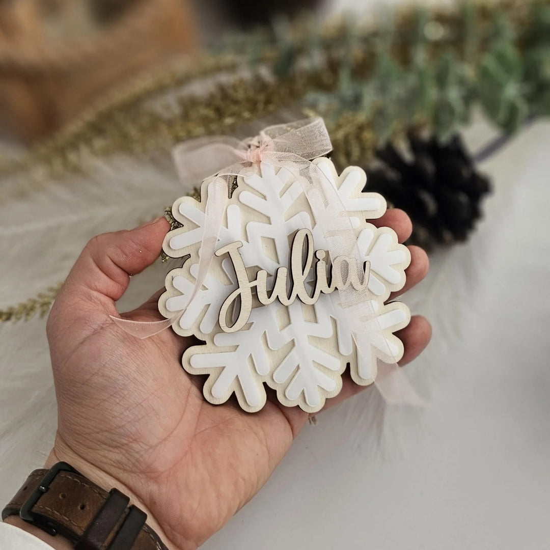 A hand holding a snowflake ornament with the name "Julia" written on it.
