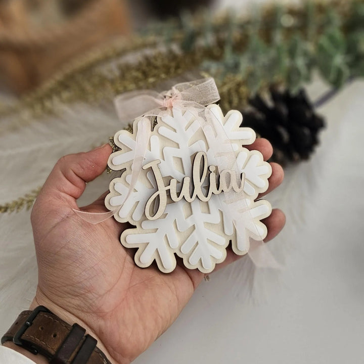 A hand holding a snowflake ornament with the name "Julia" written on it.
