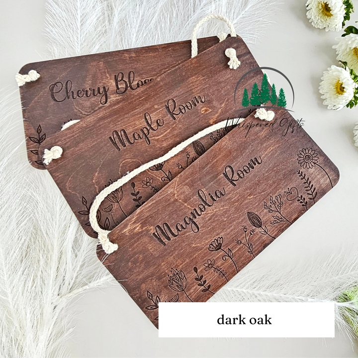 a wooden sign with the name "cherry blossom" and "maple room" written on it, along with some floral designs. The sign is placed on a white surface, and there are some white flowers in the background.