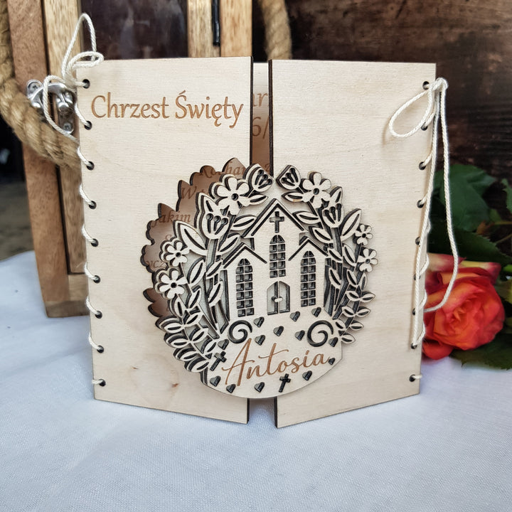 A wooden card with a decorative design featuring a house and flowers, and the name 'Antsia' written on it.