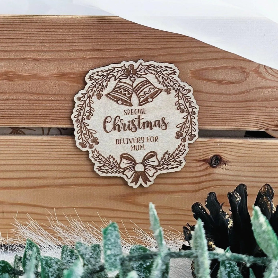 A wooden sign with a wreath and bells, along with the text "Special Christmas Delivery for Mum", is displayed on a wooden surface.