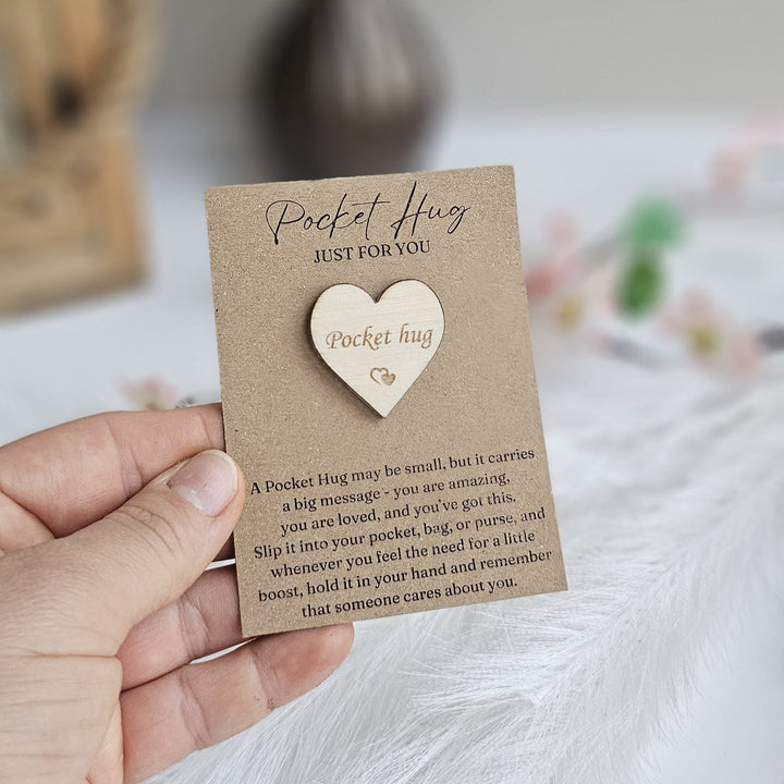 A hand holding a brown card with a wooden heart-shaped message attached to it.