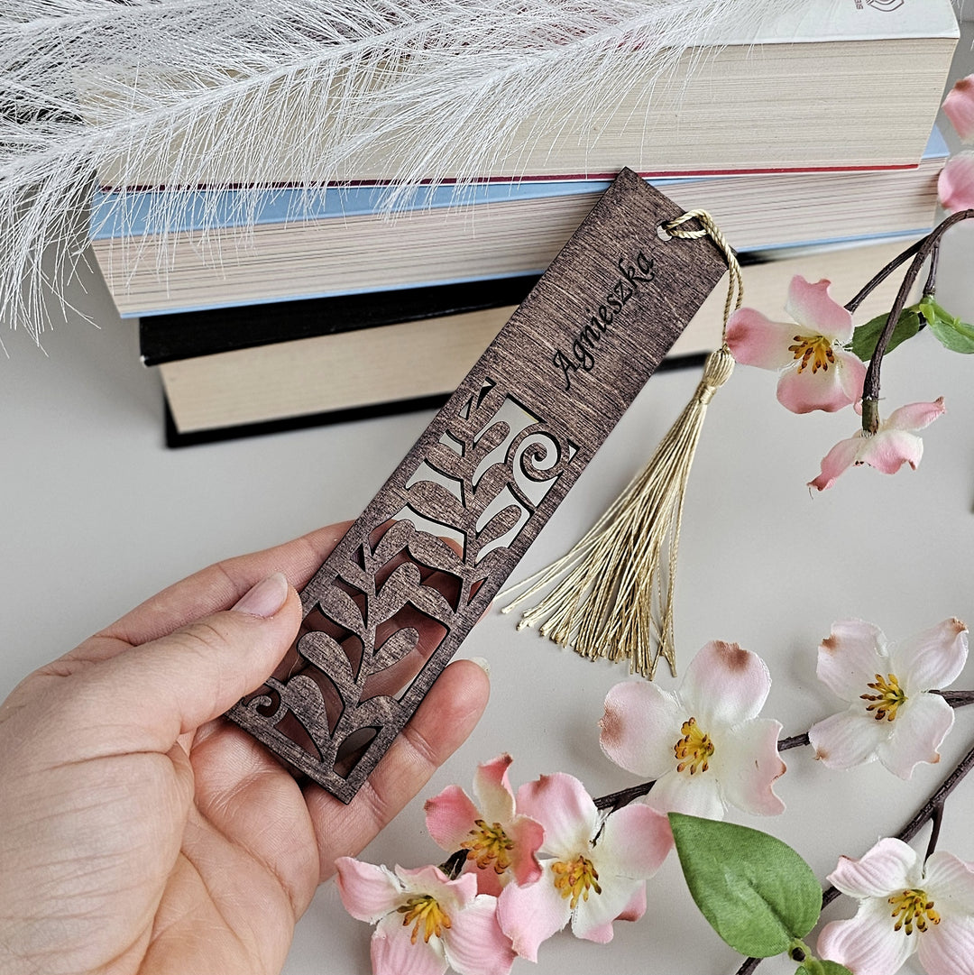 a person holding a bookmark next to some flowers