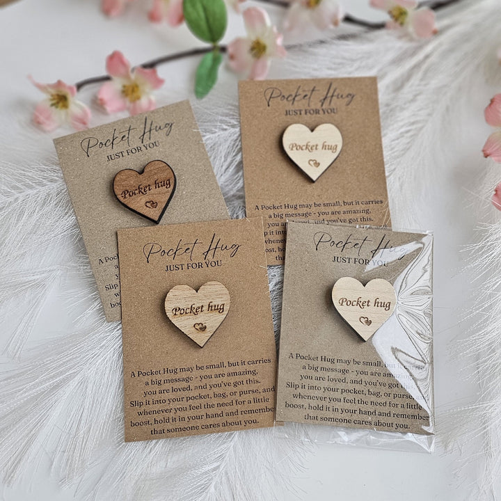 a collection of four wooden heart-shaped pins or magnets, each with a handwritten message. The pins are arranged on a white background, with some flowers visible in the background.