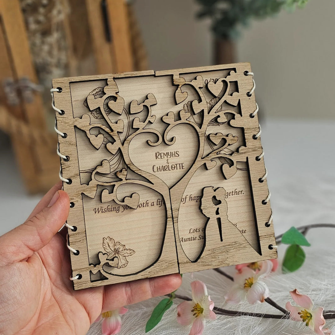 A hand is holding a wooden box with a carved design, surrounded by greenery and flowers.
