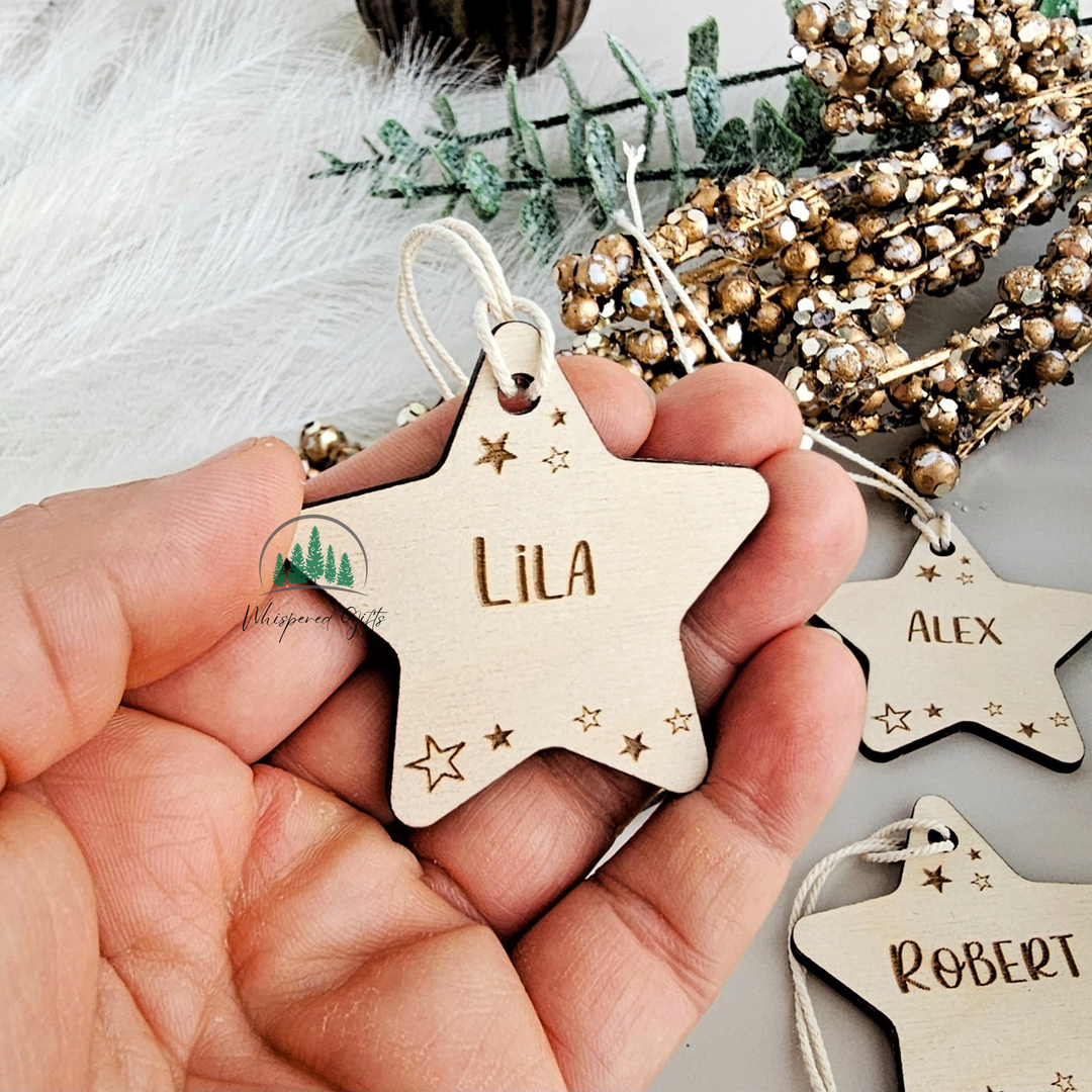 A hand holding a wooden star-shaped ornament with the name "Lila" engraved on it, surrounded by other star-shaped ornaments and greenery.