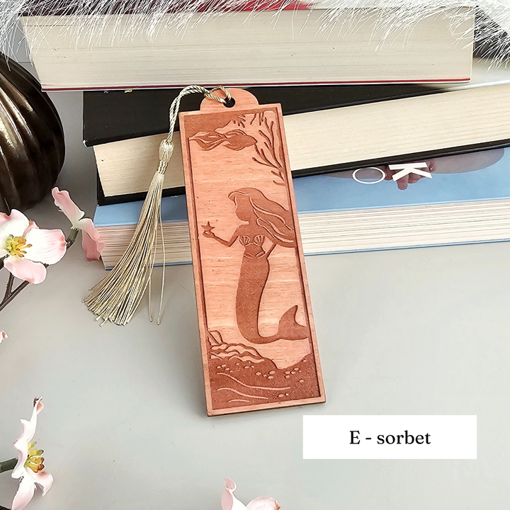 A wooden bookmark with a mermaid design, placed on top of a stack of books.