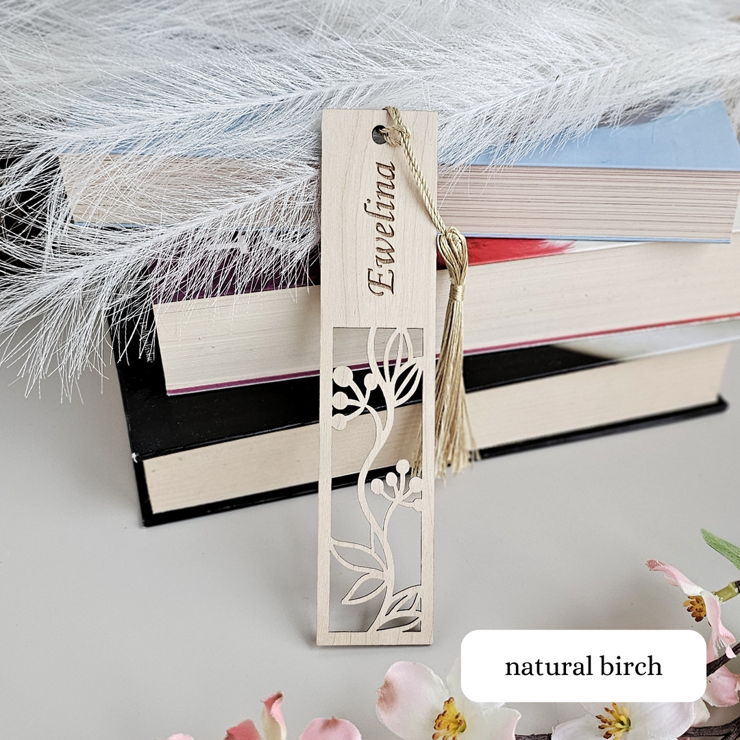 A wooden bookmark with a floral design and the name "Ewelina" engraved on it, placed on top of a stack of books.