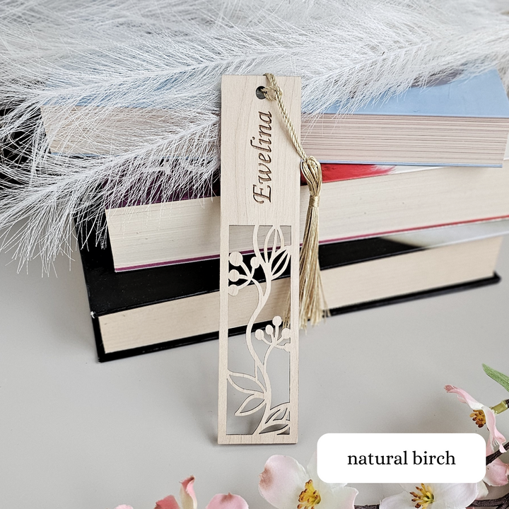 A wooden bookmark with a floral design and the name "Ewelina" engraved on it, placed on top of a stack of books.