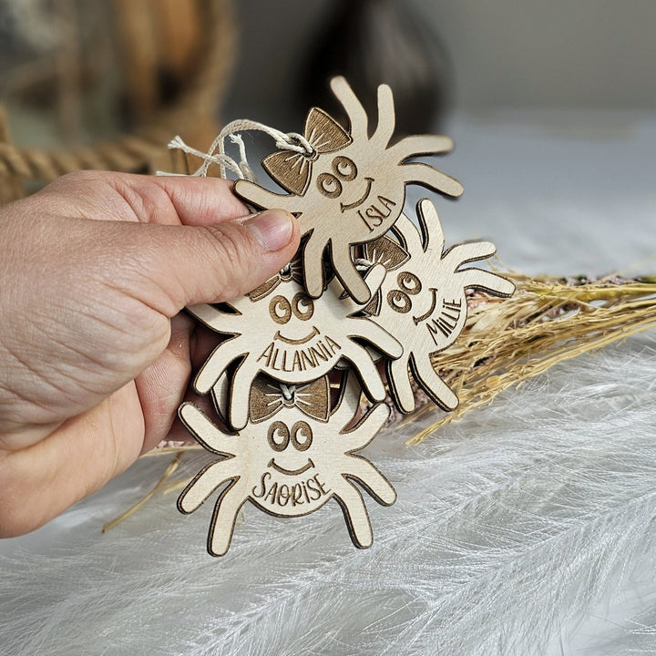 A hand is holding a set of wooden ornaments shaped like smiling spiders, with names written on them.