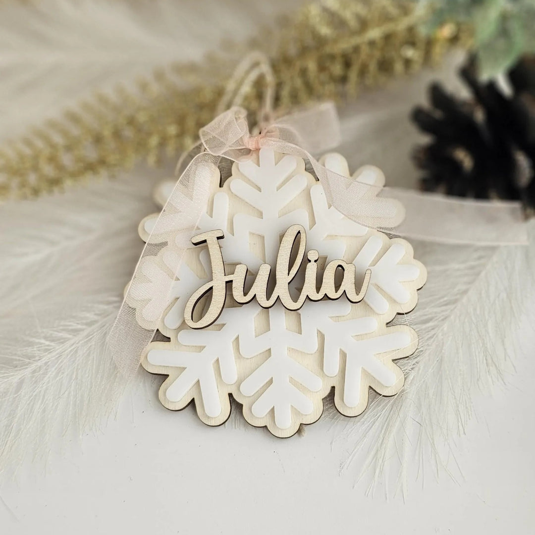 A wooden snowflake ornament with the name "Julia" written on it, placed on a white surface with some feathers in the background.
