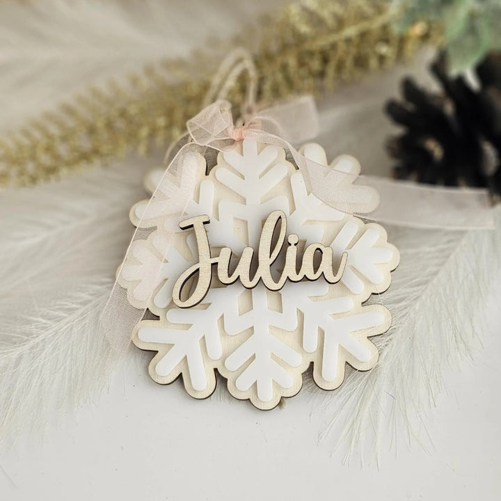 A wooden snowflake ornament with the name "Julia" written on it, placed on a white surface with some feathers in the background.