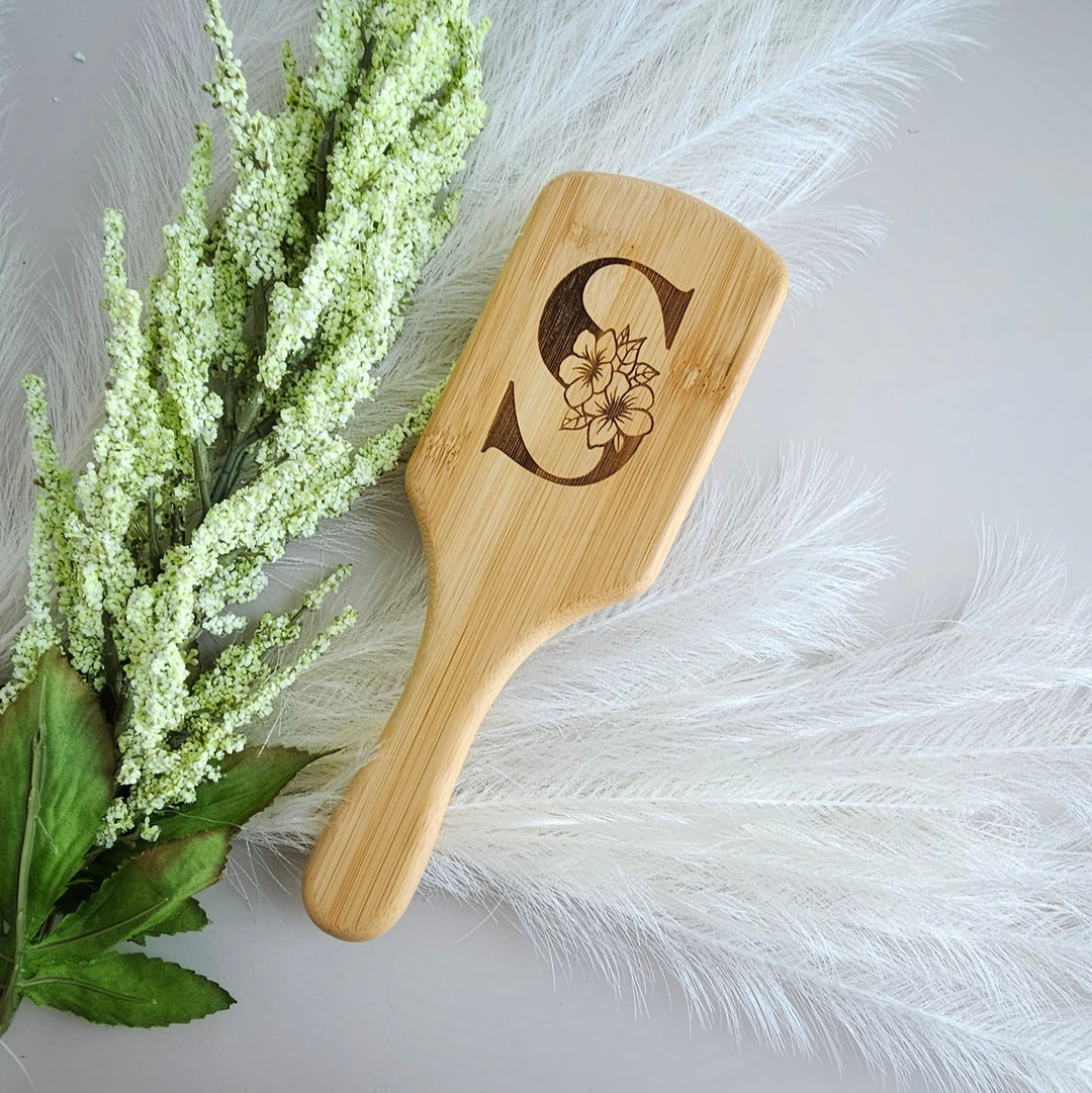 A wooden brush with a floral design on it, placed next to a bunch of white flowers and feathers.