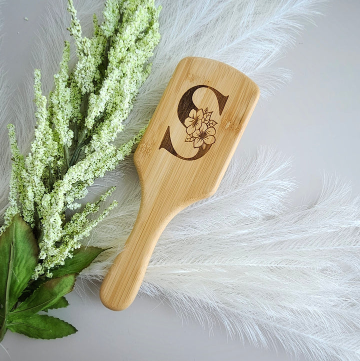 A wooden brush with a floral design on it, placed next to a bunch of white flowers and feathers.