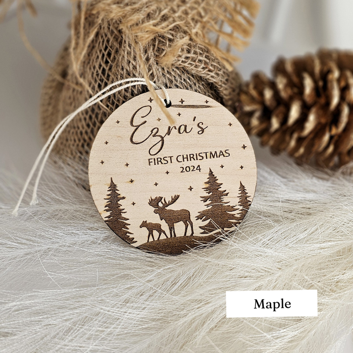 A wooden ornament with a deer silhouette and a starry night sky, labeled "Ezra's FIRST CHRISTMAS 2024" and "Maple"